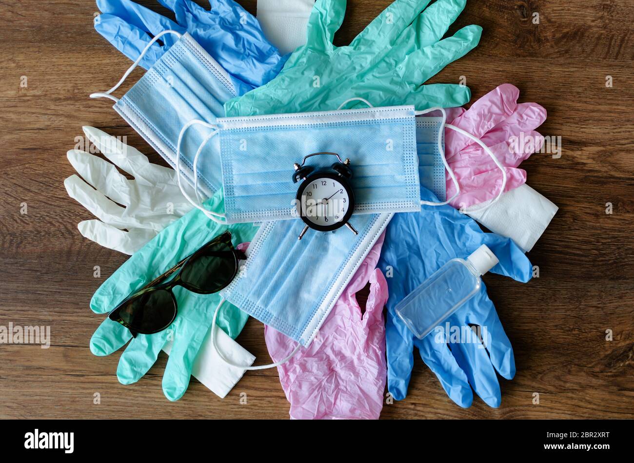 maschere mediche e sveglia, guanti in gomma e disinfettante, attrezzature di protezione su sfondo in legno, primo piano Foto Stock