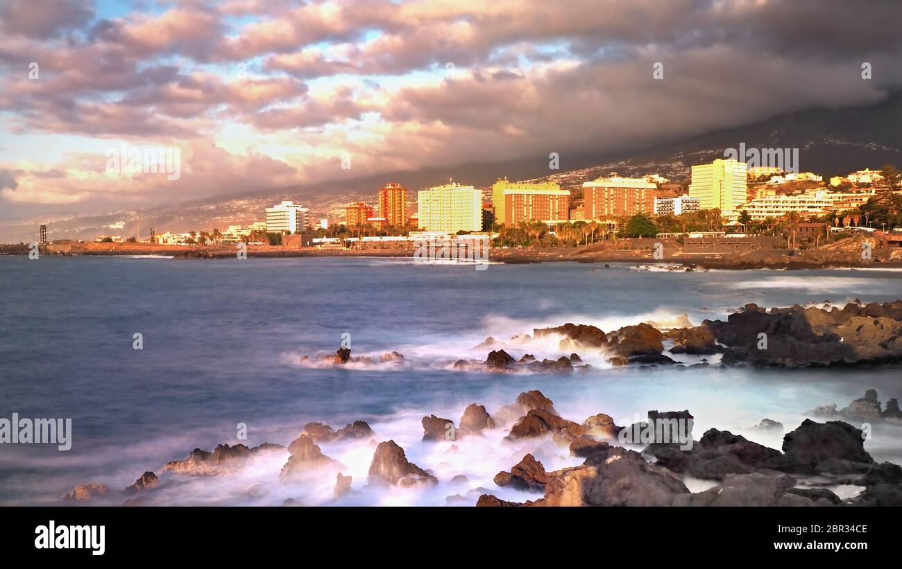 Vista di Puerto de la Cruz al crepuscolo sulle rocce laviche dell'Atlantico, fotografate utilizzando filtri ND. Il cielo ha nuvole scure provenienti dalla montagna Foto Stock