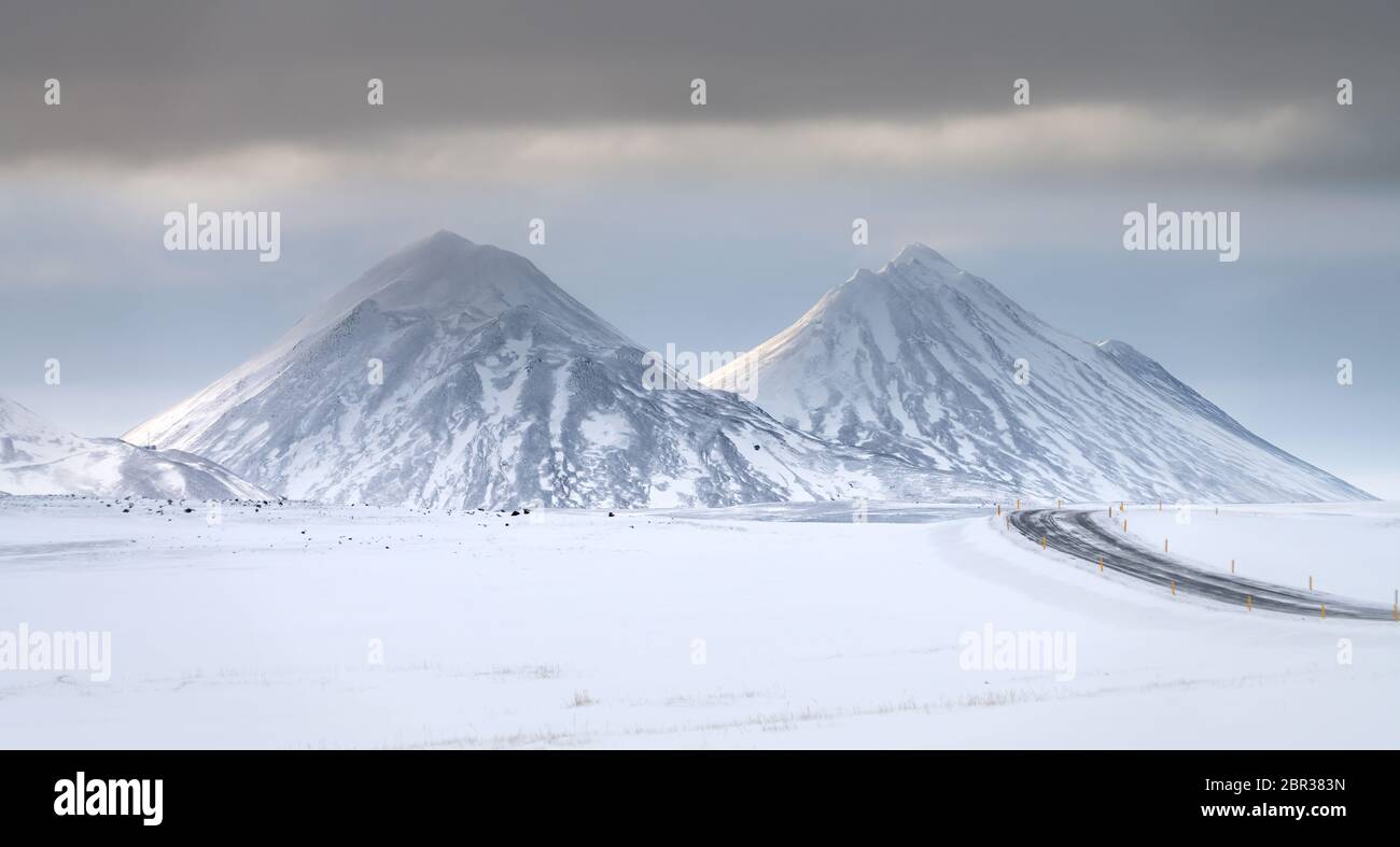 Twin neve coperta di sole cime vulcaniche vicino al Lago Myvatn, Islanda del Nord con strada in inverno Foto Stock