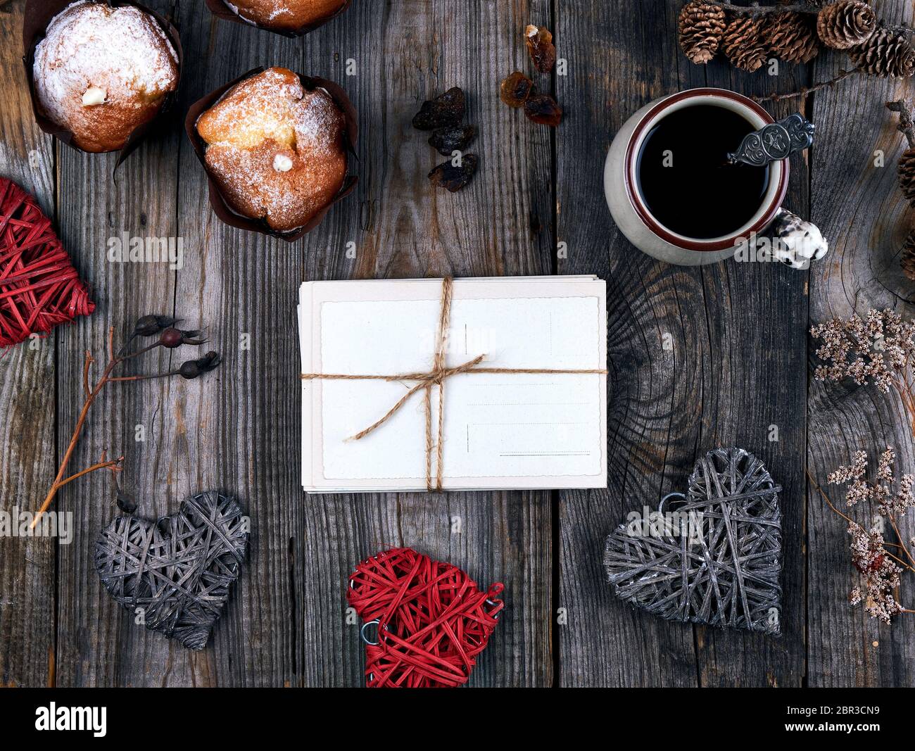 Vecchie cartoline di carta legato con una corda su un grigio Sfondo di legno, vista dall'alto, accanto a una tazza di caffè e muffin cotti al forno Foto Stock