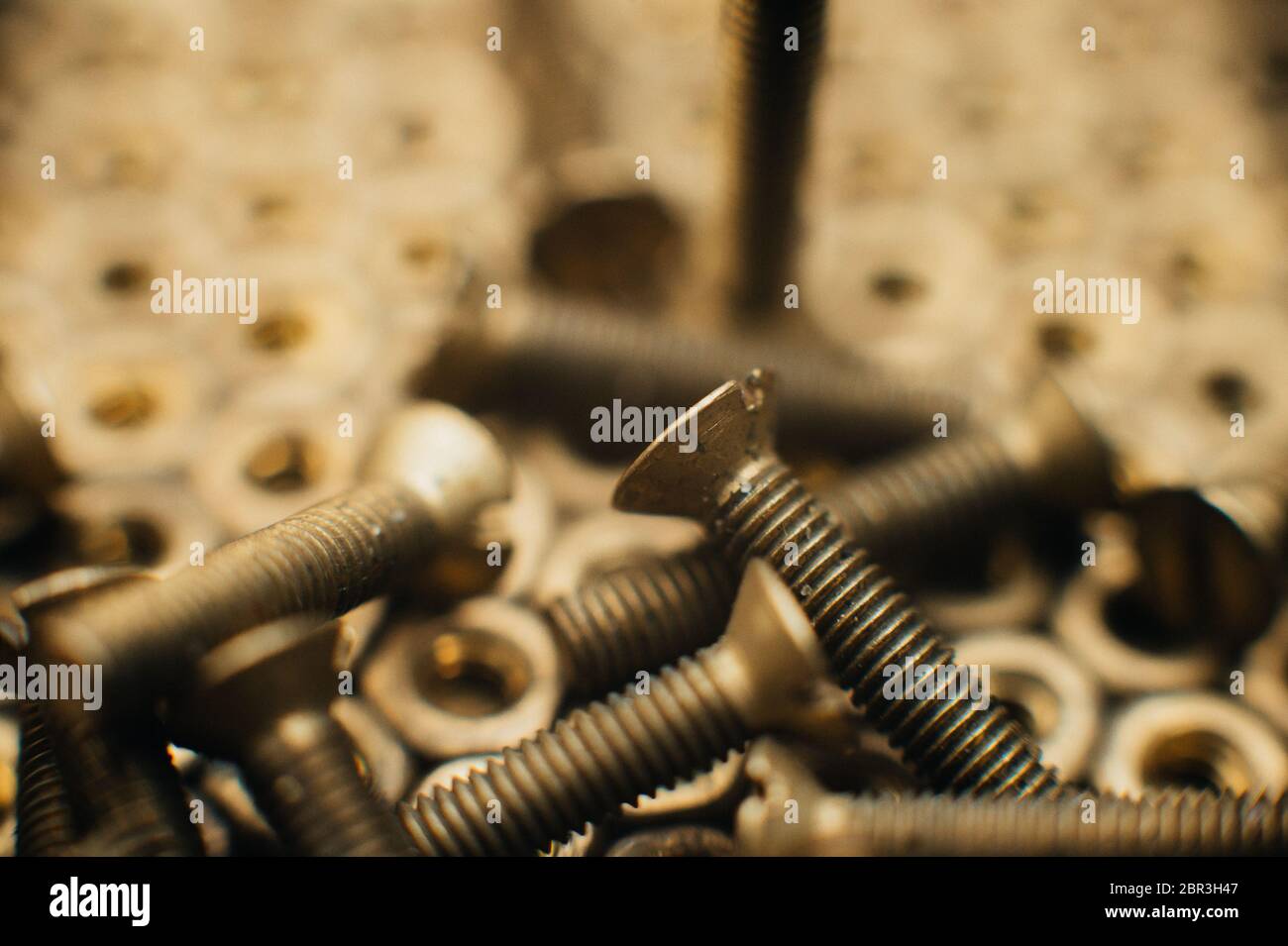 Primo piano, macro. Vecchie viti a testa svasata in ottone sovietico con un cacciavite a testa piatta. Struttura, fondo di noci di ottone disposte in forma di hone Foto Stock