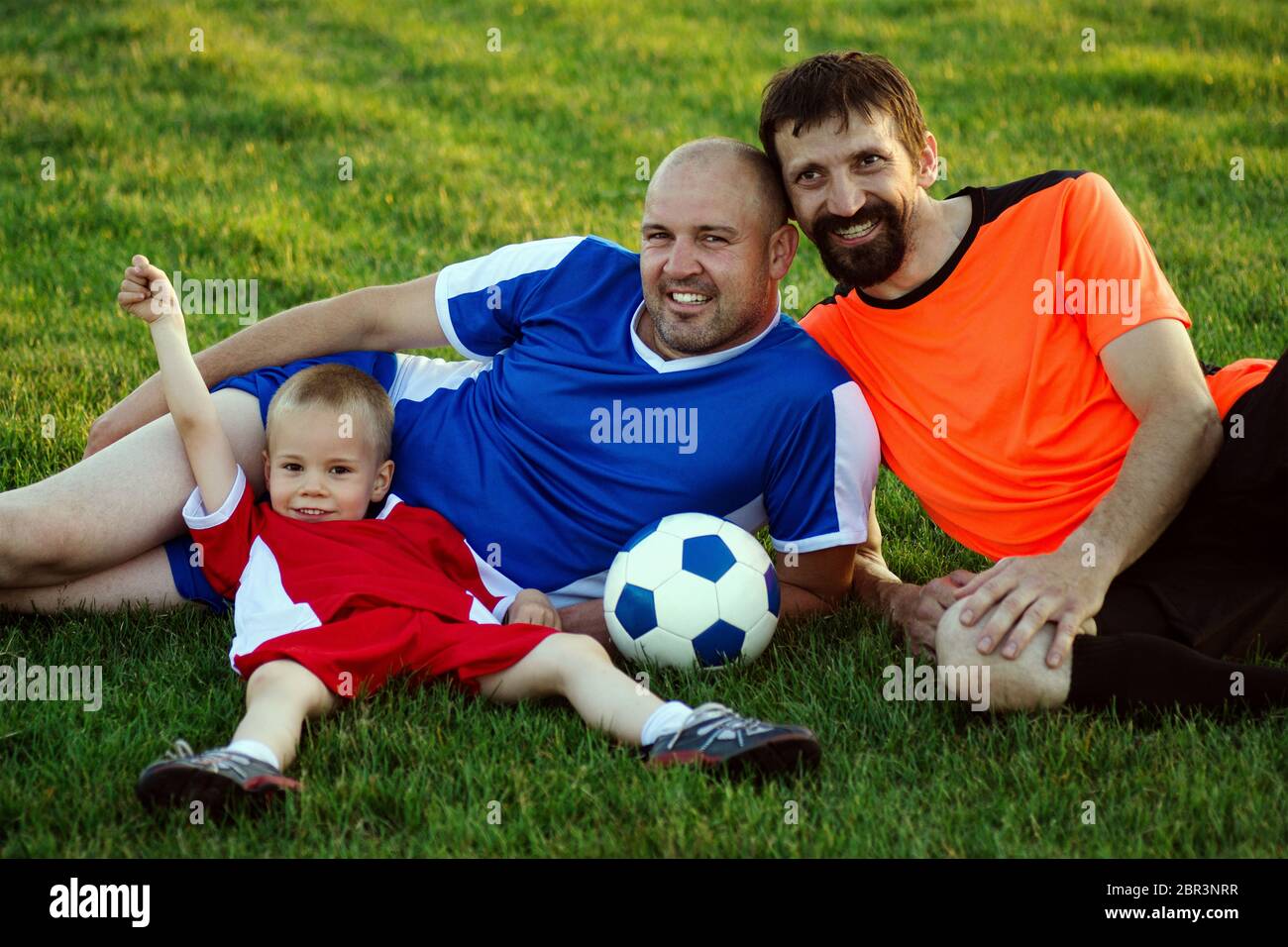 Padre, figlio e zio della famiglia di calcio sono in abbigliamento sportivo di calcio sdraiato sull'erba in campo da gioco e in posa. Famiglia felice nel concetto di sport. Foto Stock