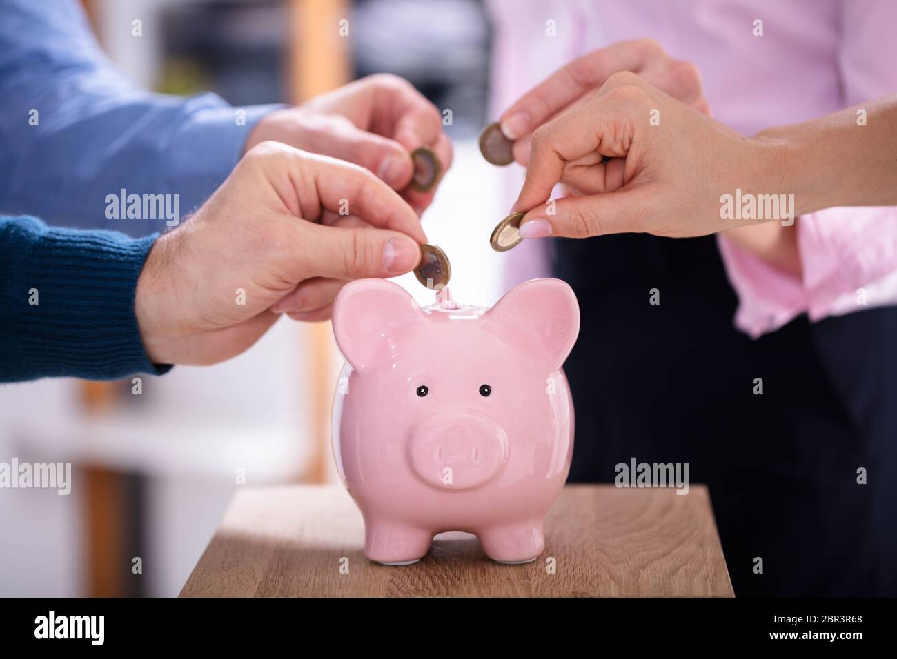Gli imprenditori di mano inserire monete in rosa Piggybank in Office Foto Stock