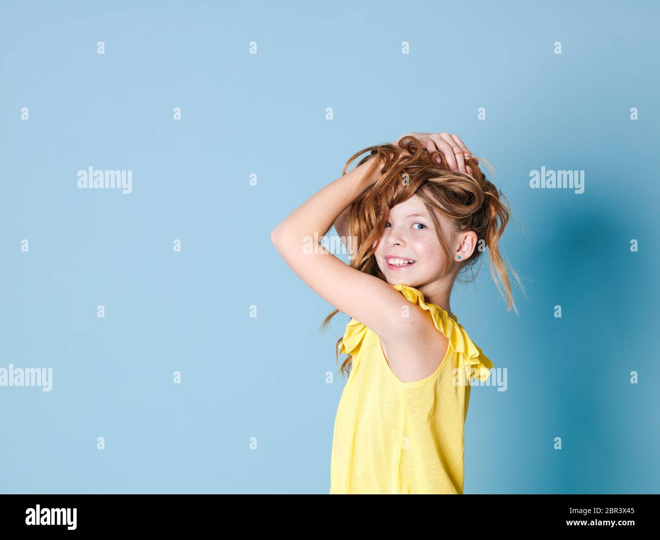 Bella ragazza con i capelli bruna con la parte superiore gialla è in posa di fronte a sfondo blu Foto Stock