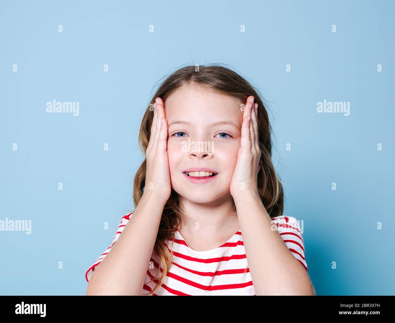 Bella ragazza con i capelli ricci e rosso bianco striped shirt è in posa di fronte di sfondo blu Foto Stock