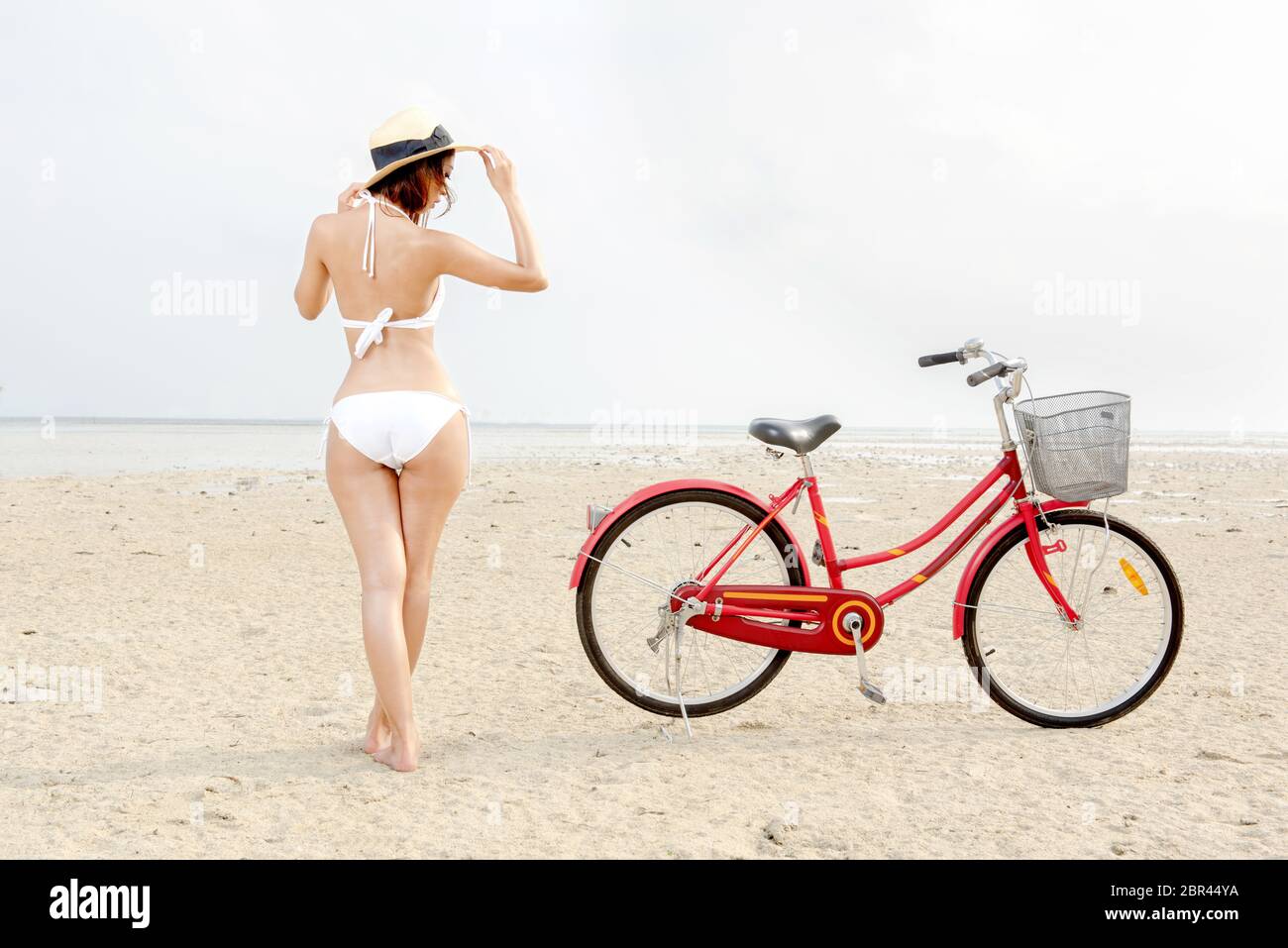 Vista posteriore di asian sexy ragazza con cappello e bikini con la bici sulla spiaggia. Vacanze estive Foto Stock