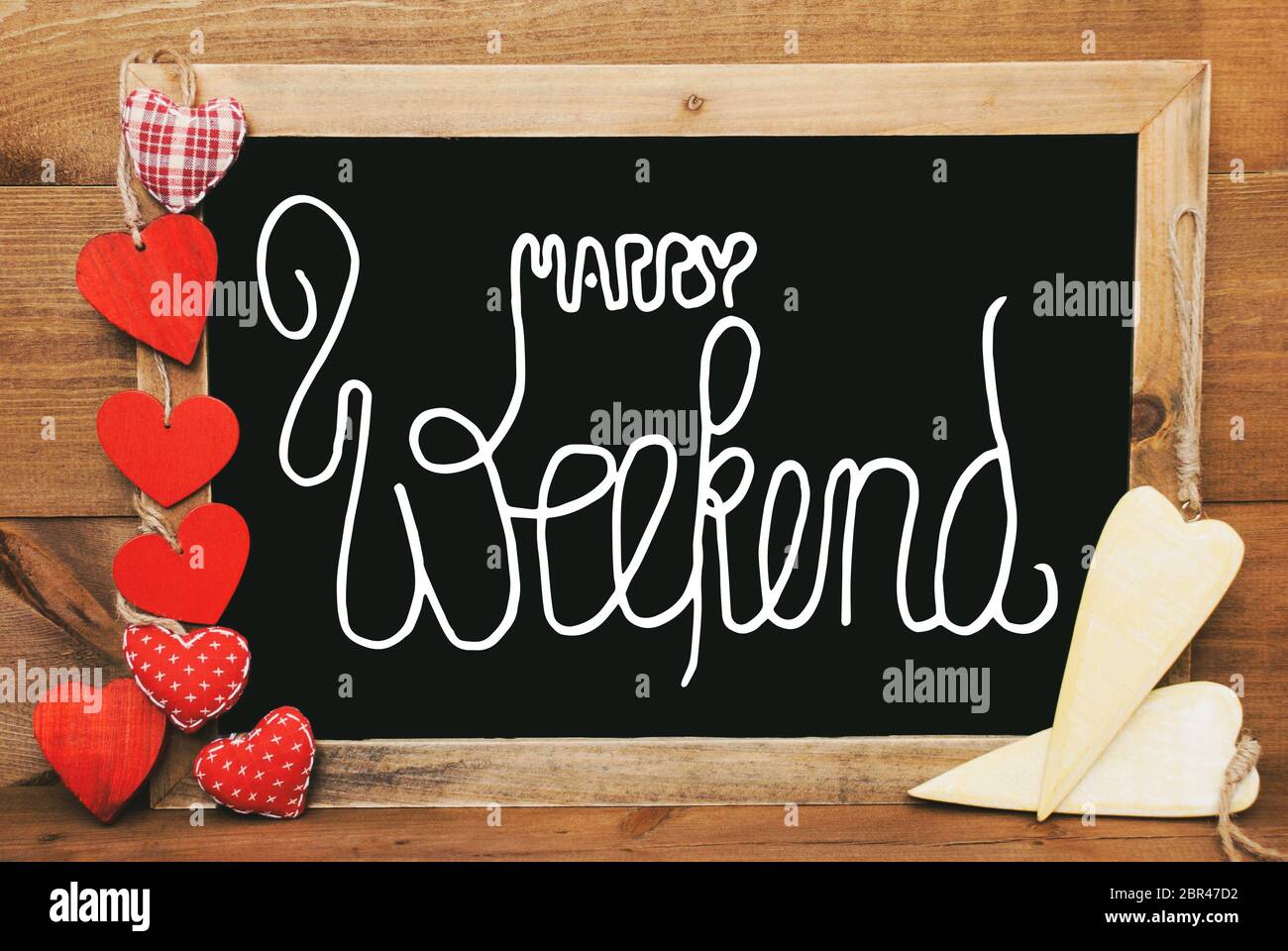 Lavagna con la calligrafia inglese Happy Weekend. Tessile di rosso e giallo in legno cuori. Sfondo di legno con l'annata, rustico o in stile retrò. Foto Stock