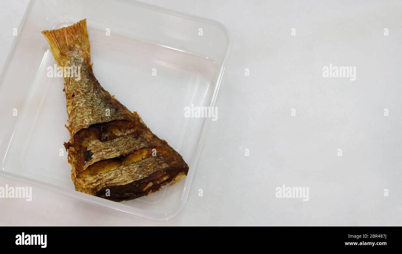 La coda di un pesce fritto, posto in un contenitore di plastica. Spazio di copia a destra. Foto Stock