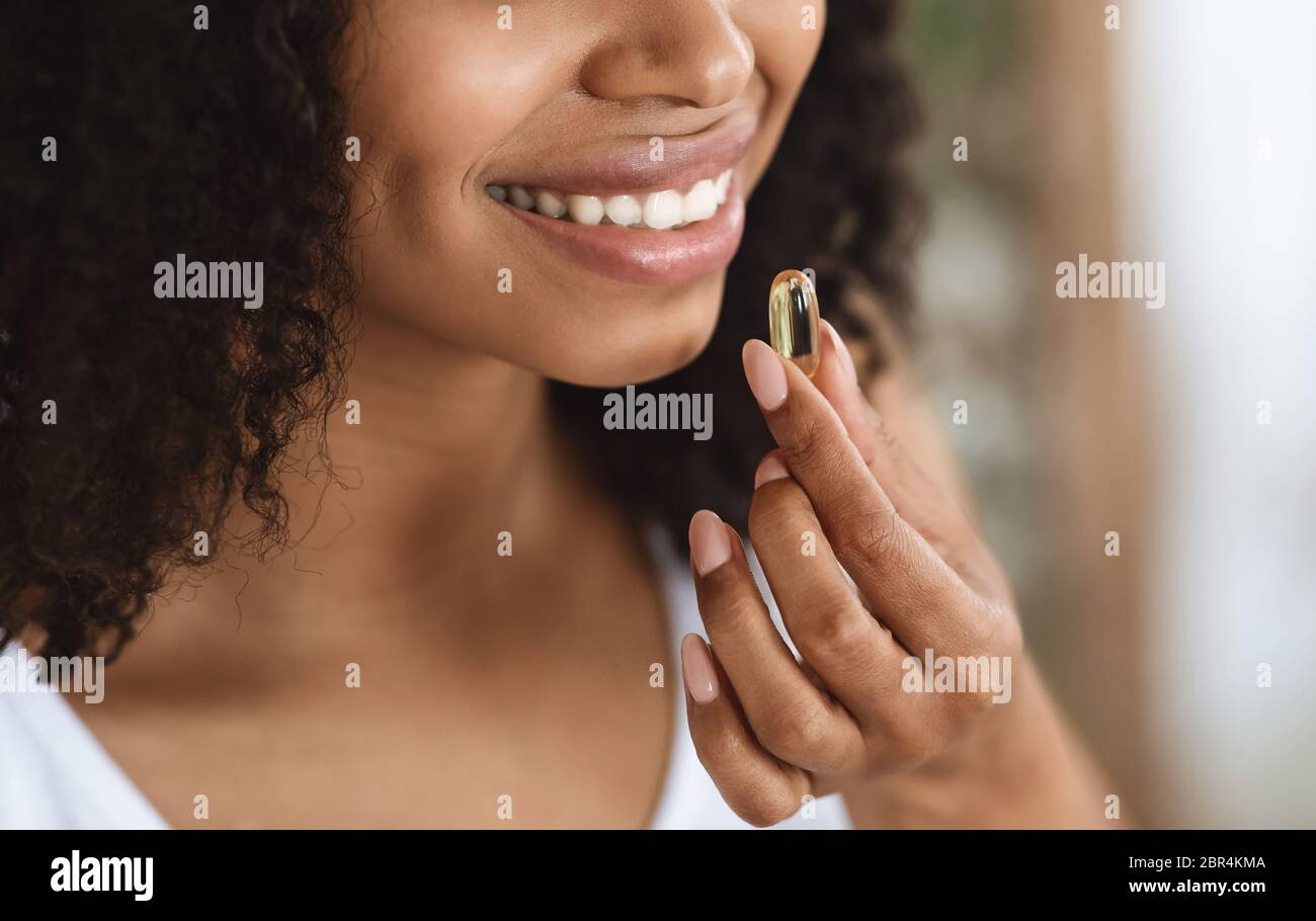 Supplemento bellezza. Primo piano di sorridente donna Nera prendendo capsula di vitamina pill Foto Stock
