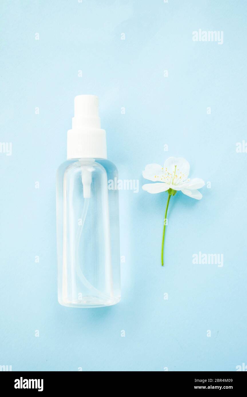 Bottiglia antisettica a mano e fiore di ciliegio fiorito beatful su sfondo blu. Arrestare il concetto di coronavirus. Foto Stock