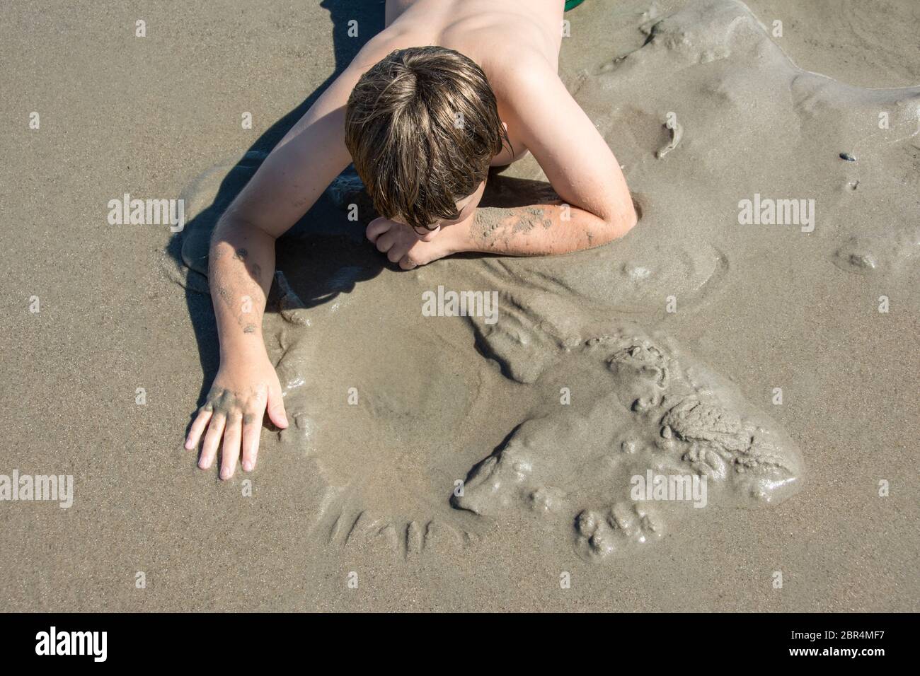 Ragazzo che fa stampe a mano sulla sabbia in spiaggia Foto Stock