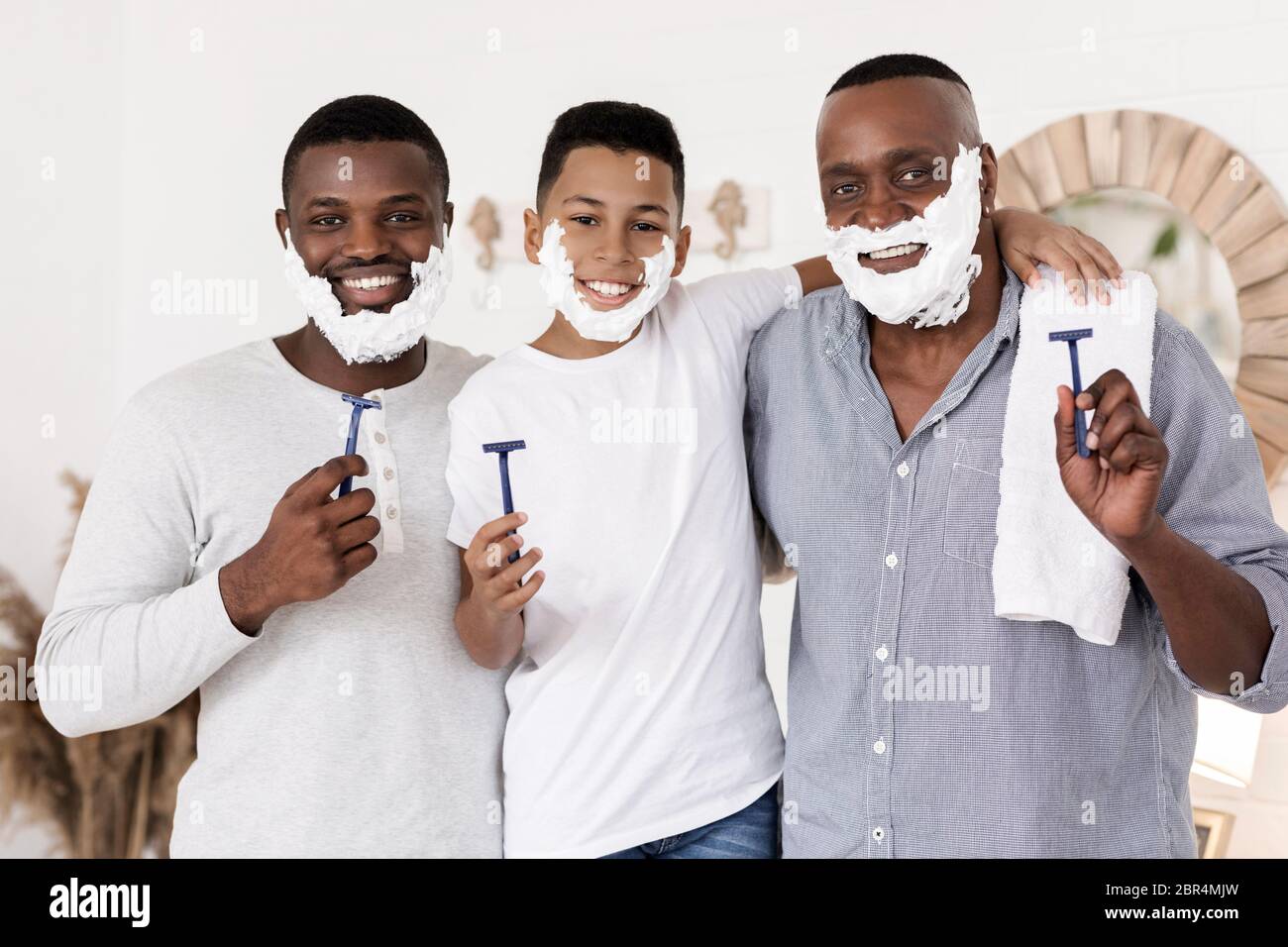 Tre uomini generazionali si radono insieme in bagno e sorridono alla macchina fotografica Foto Stock