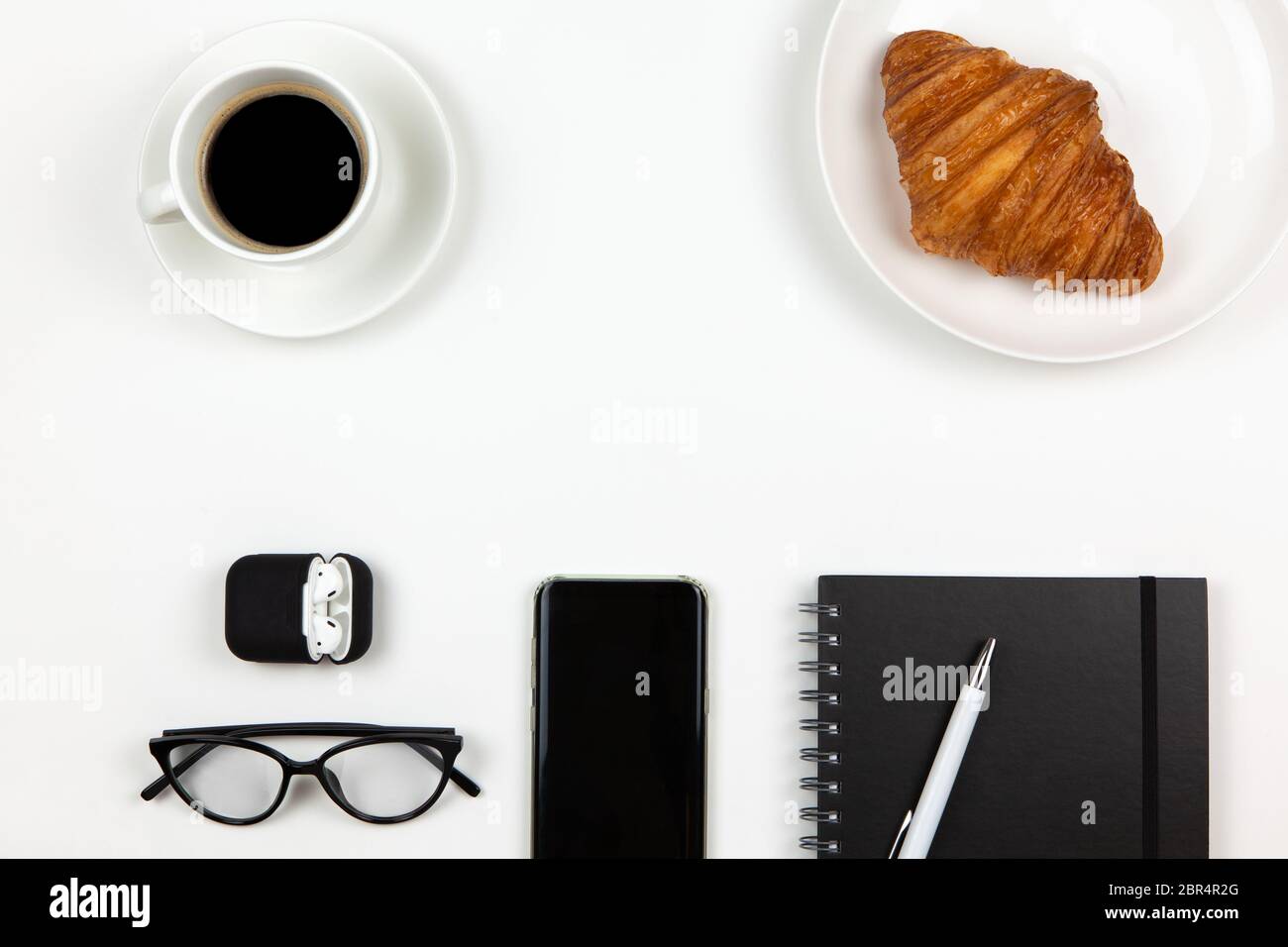 Moderno spazio di lavoro di freelance. Smartphone, caffè, notebook, penna, croissant, occhiali, cuffie in custodia su sfondo bianco, spazio per la copia, piatto l Foto Stock