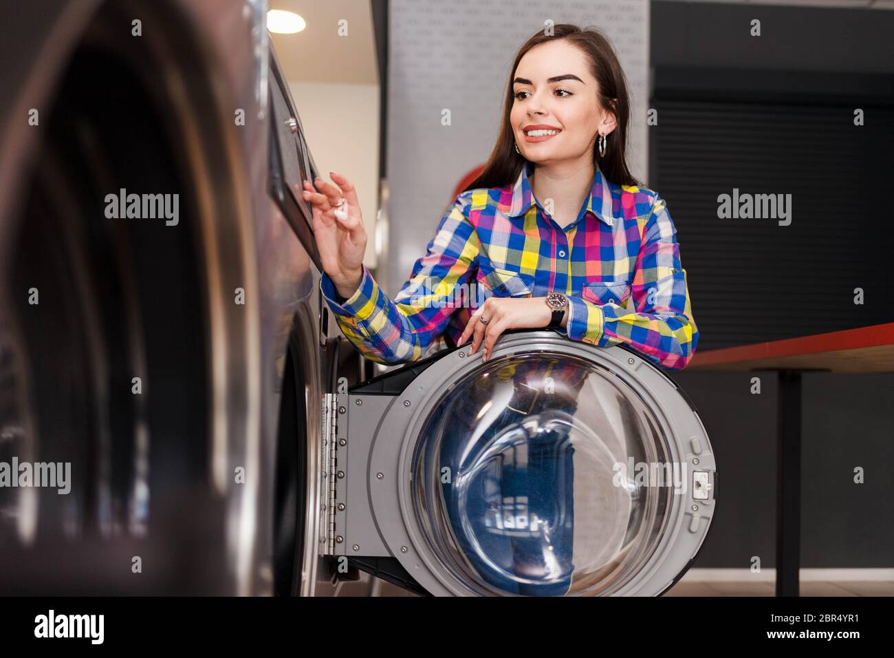 Donna si appoggiò alla porta della lavatrice alla lavanderia self-service. Il concetto di lavanderia automatica è soddisfatto Foto Stock