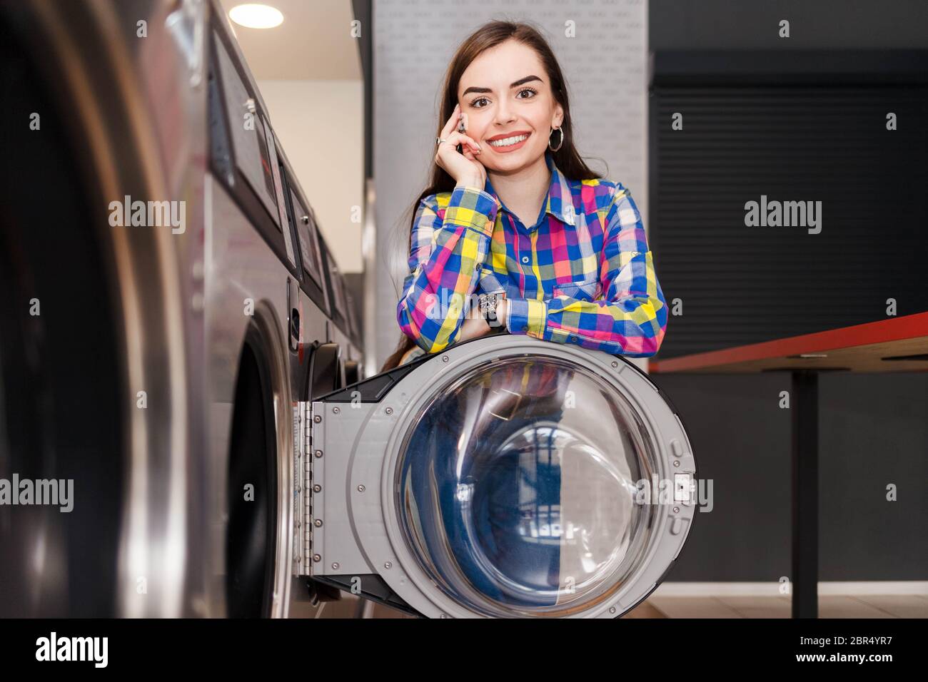 Donna si appoggiò alla porta della lavatrice alla lavanderia self-service. Il concetto di lavanderia automatica è soddisfatto Foto Stock