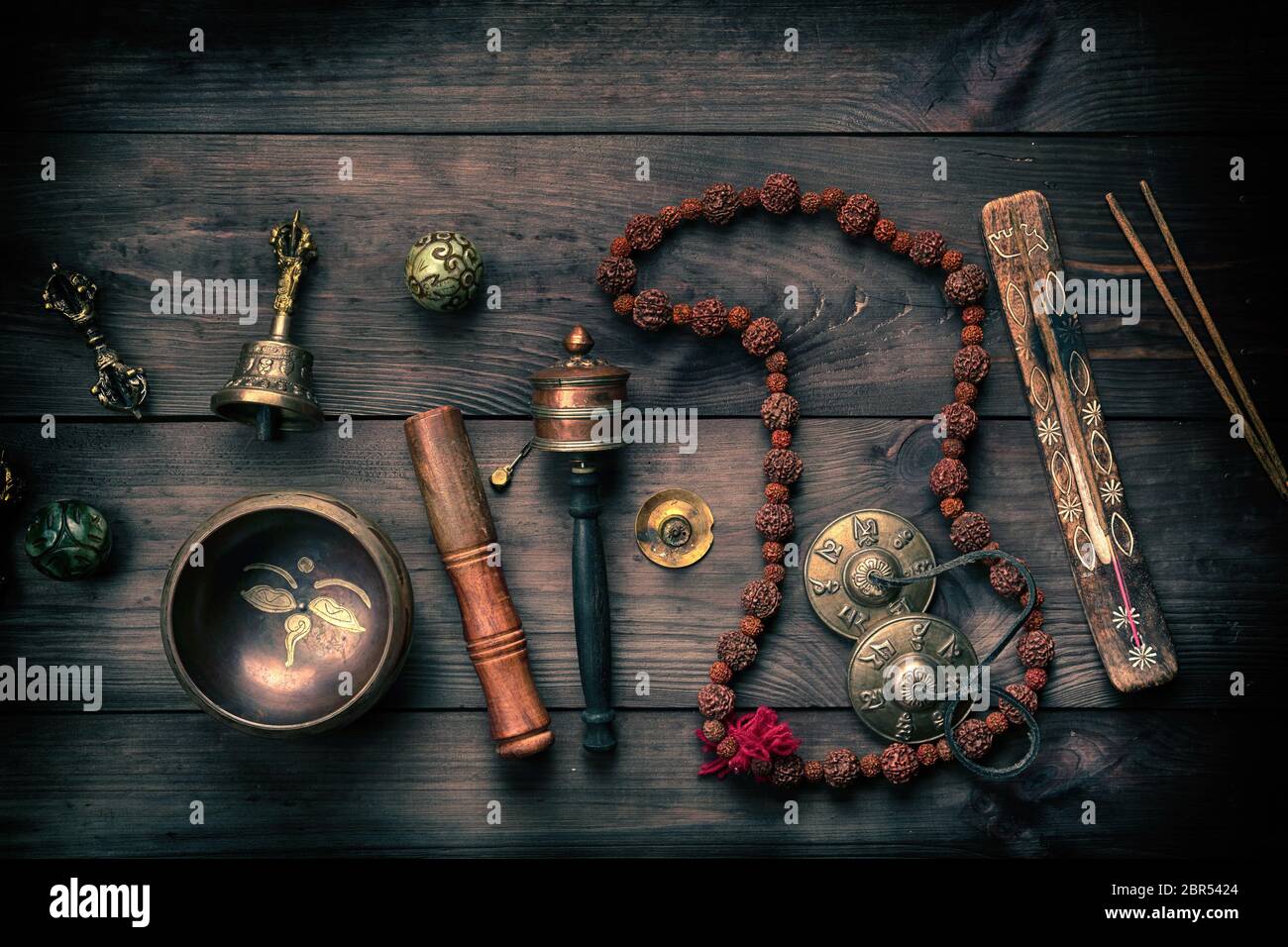 Il rame Singing Bowl, grani di preghiera, preghiera tamburo e altre religiose tibetane oggetti per la meditazione e la medicina alternativa su un legno marrone backgroun Foto Stock