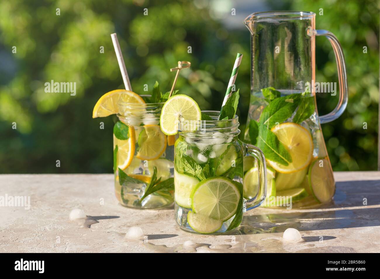 Decanter e due bicchieri di limonata o mojito, cocktail con limone, cetriolo e menta, bevanda rinfrescante fredda o bevanda con ghiaccio e paglia di carta, ou Foto Stock