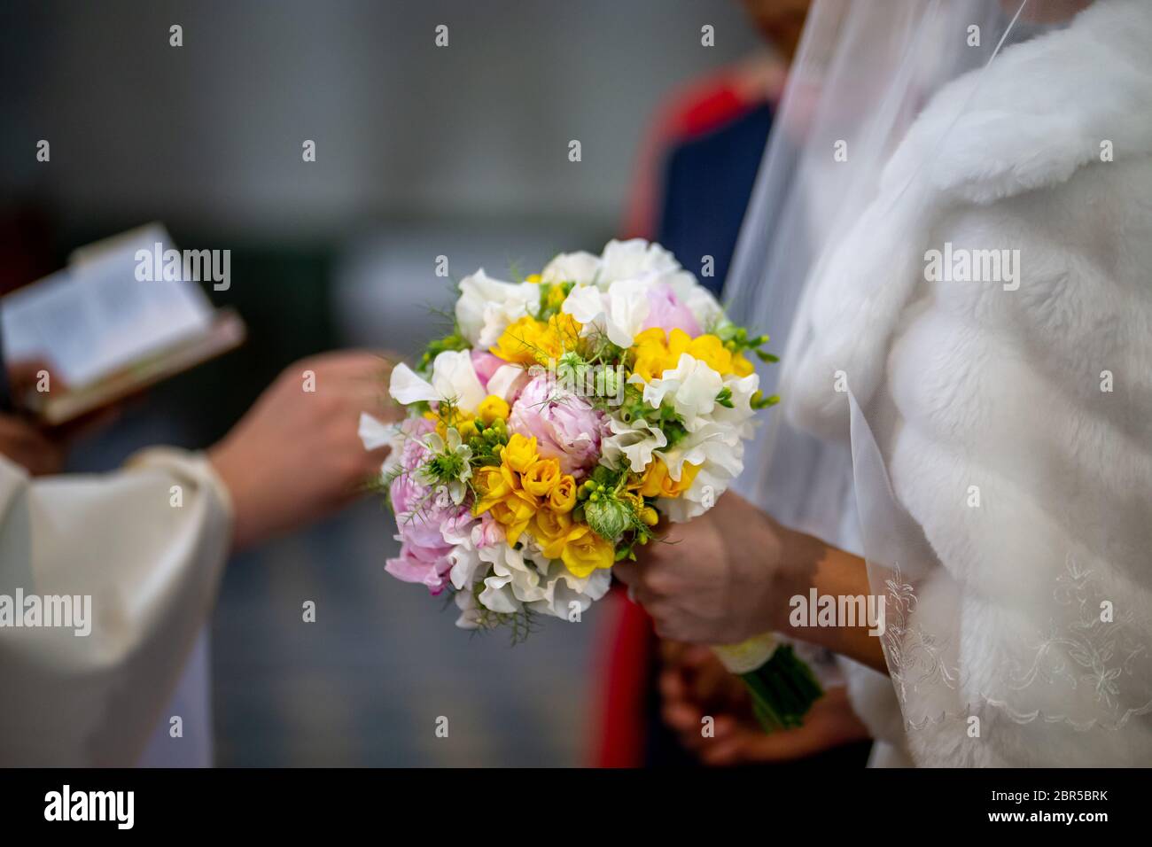 La sposa detiene un matrimonio bouquet di fiori nella sua mano. Il bouquet è composto di bianco, giallo e fiori di colore rosa. Sacerdote e spose mani è Foto Stock