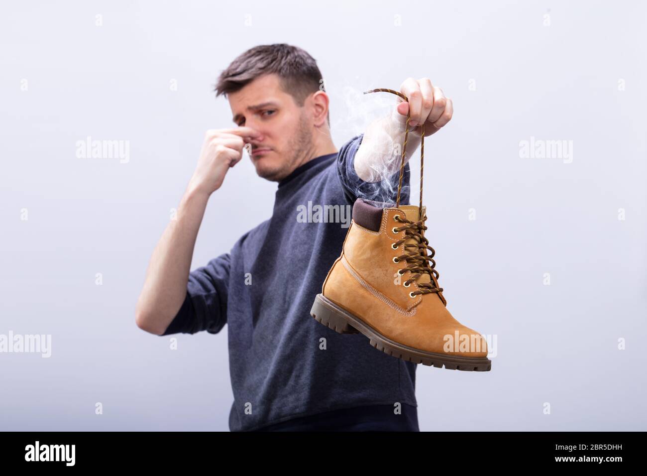 Close-up di un uomo che copre il suo naso tenendo Stinky calzatura contro uno sfondo bianco Foto Stock