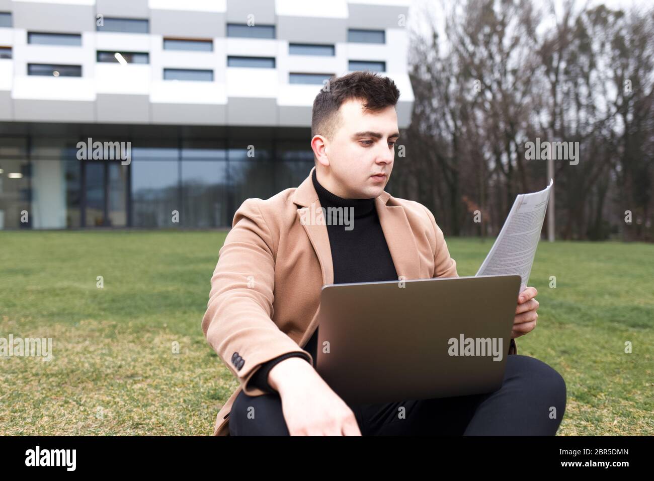 L'uomo sta studiando mentre si siede con un taccuino in mano sull'erba vicino all'università Foto Stock
