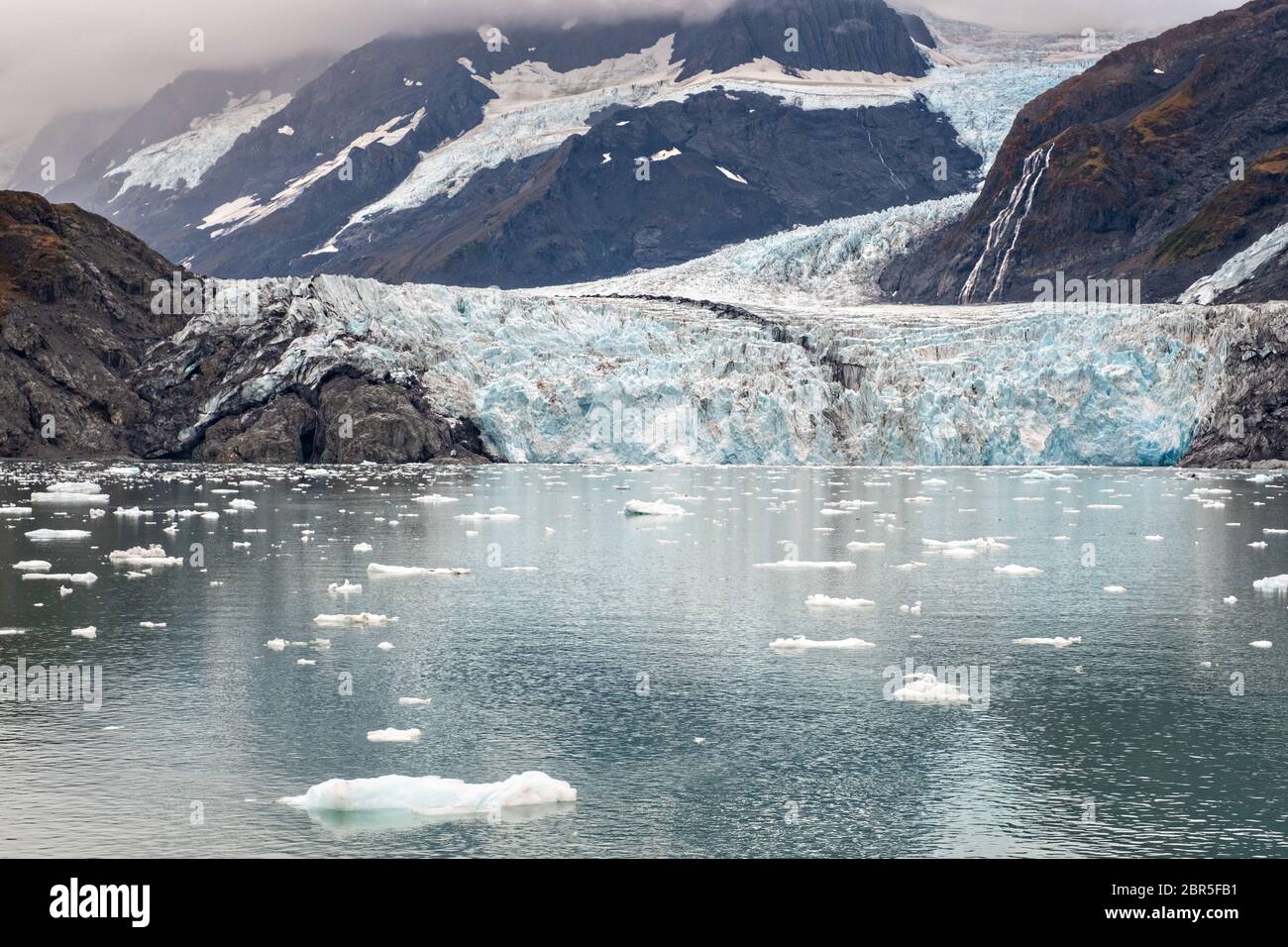 Il ghiacciaio a sorpresa con la morena mediale che corre lungo il centro e ghiaccio di brash galleggianti nel fiordo Harriman, vicino a Whittier, Alaska. Il ghiacciaio Surprise è il più attivo ghiacciaio di acqua di mare calvente del Prince William Sound. Foto Stock