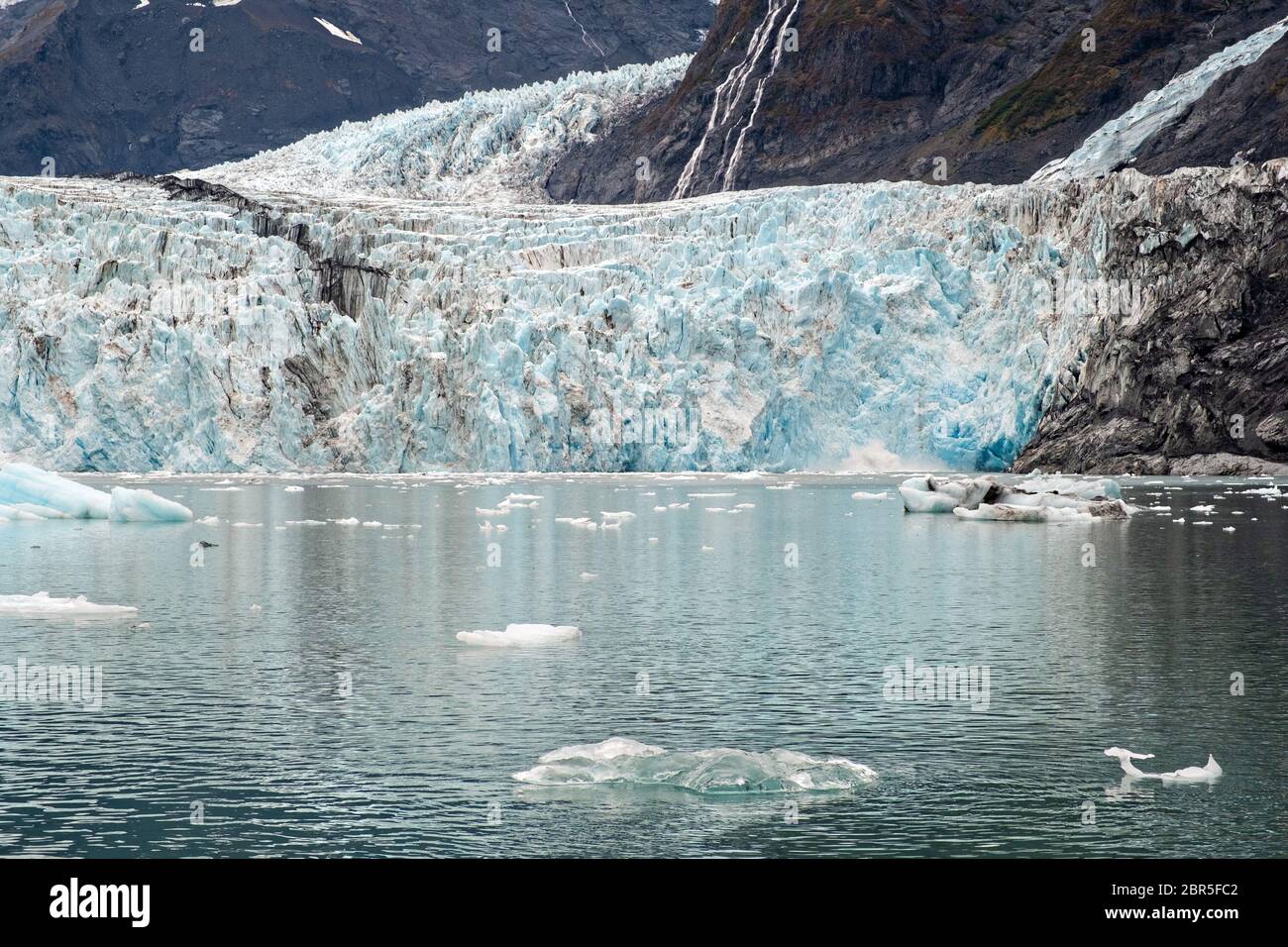 Il ghiacciaio a sorpresa con la morena mediale che corre lungo il centro e ghiaccio di brash galleggianti nel fiordo Harriman, vicino a Whittier, Alaska. Il ghiacciaio Surprise è il più attivo ghiacciaio di acqua di mare calvente del Prince William Sound. Foto Stock