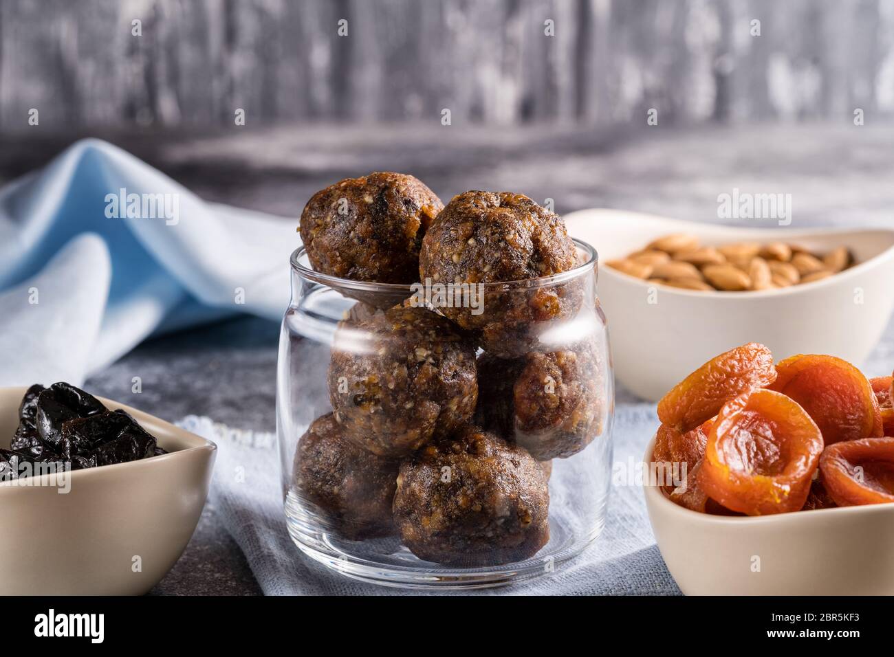 Palle energetiche di frutta secca e noci in un vaso di vetro, accanto agli ingredienti per cucinare albicocche secche, prugne, mandorle. Il concetto di vega sano Foto Stock