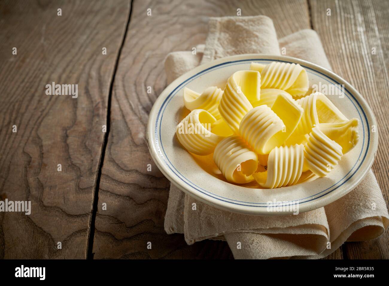 Bobine decorativo di farm burro fresco su un piatto bilanciato sulla parte superiore di un tovagliolo su una tavola in legno rustico con grana di legno a trama e spazio di copia Foto Stock