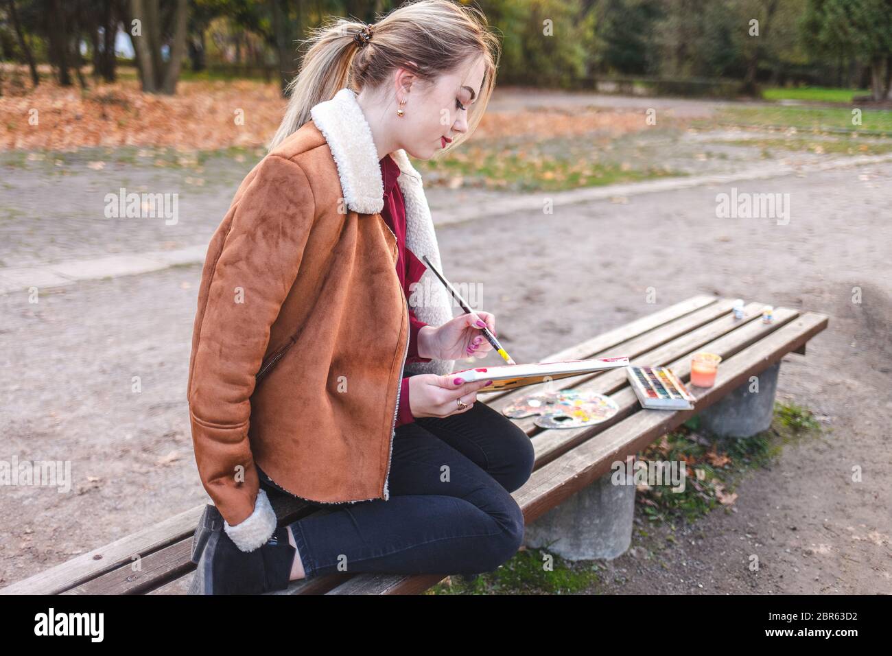 Ritratto di una giovane artista ragazza che siede su una panchina e disegna un quadro Foto Stock