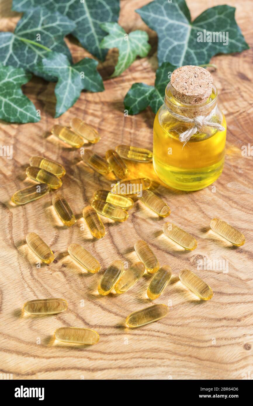 Capsule oblunghe gelatinose trasparenti di olio di pesce sono state sparse sullo sfondo di legno. Acidi grassi polinsaturi Omega-3-essenziali. Semi di lino oi Foto Stock