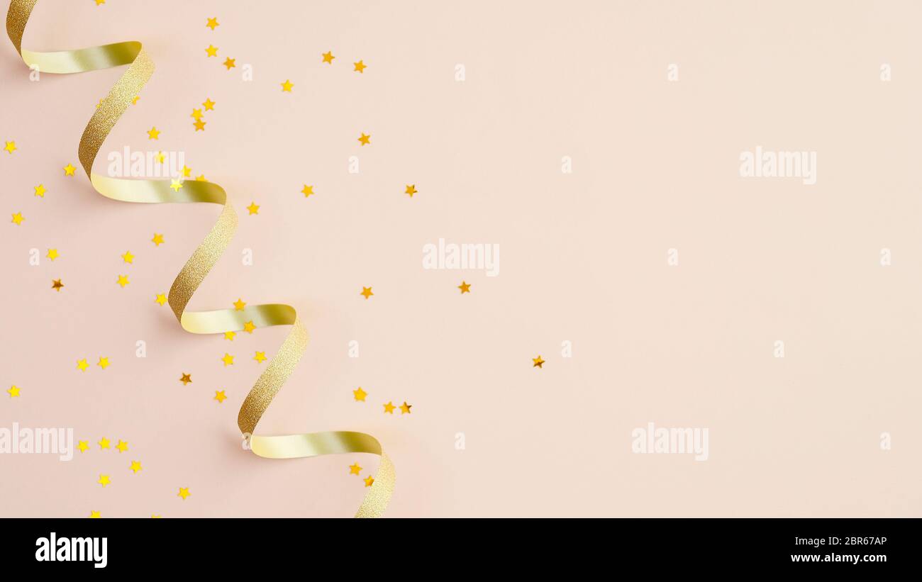 Nastro a spirale dorato e stella di confetti su sfondo beige. Natale, compleanno o matrimonio. Disposizione piatta, vista dall'alto. Foto Stock