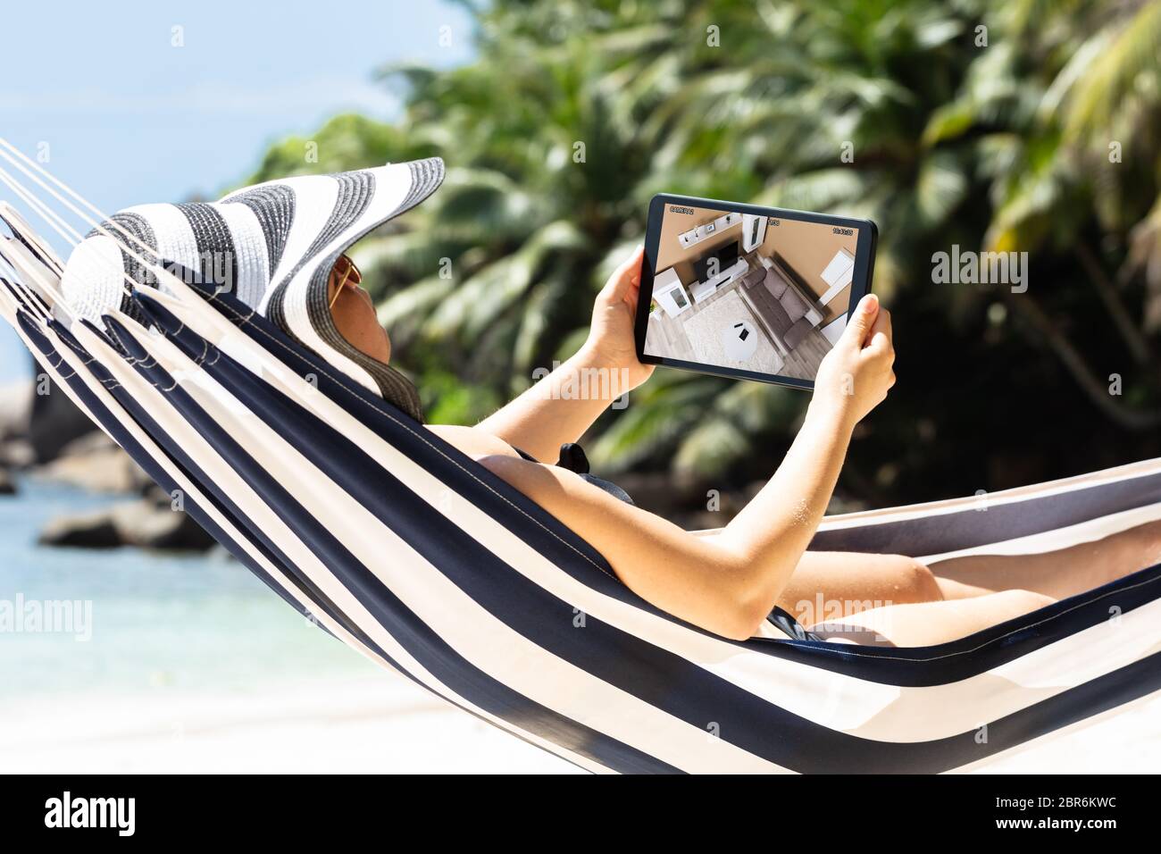 Donna sdraiata su amaca telecamere di sorveglianza in Live View sulla tavoletta digitale presso la spiaggia Foto Stock