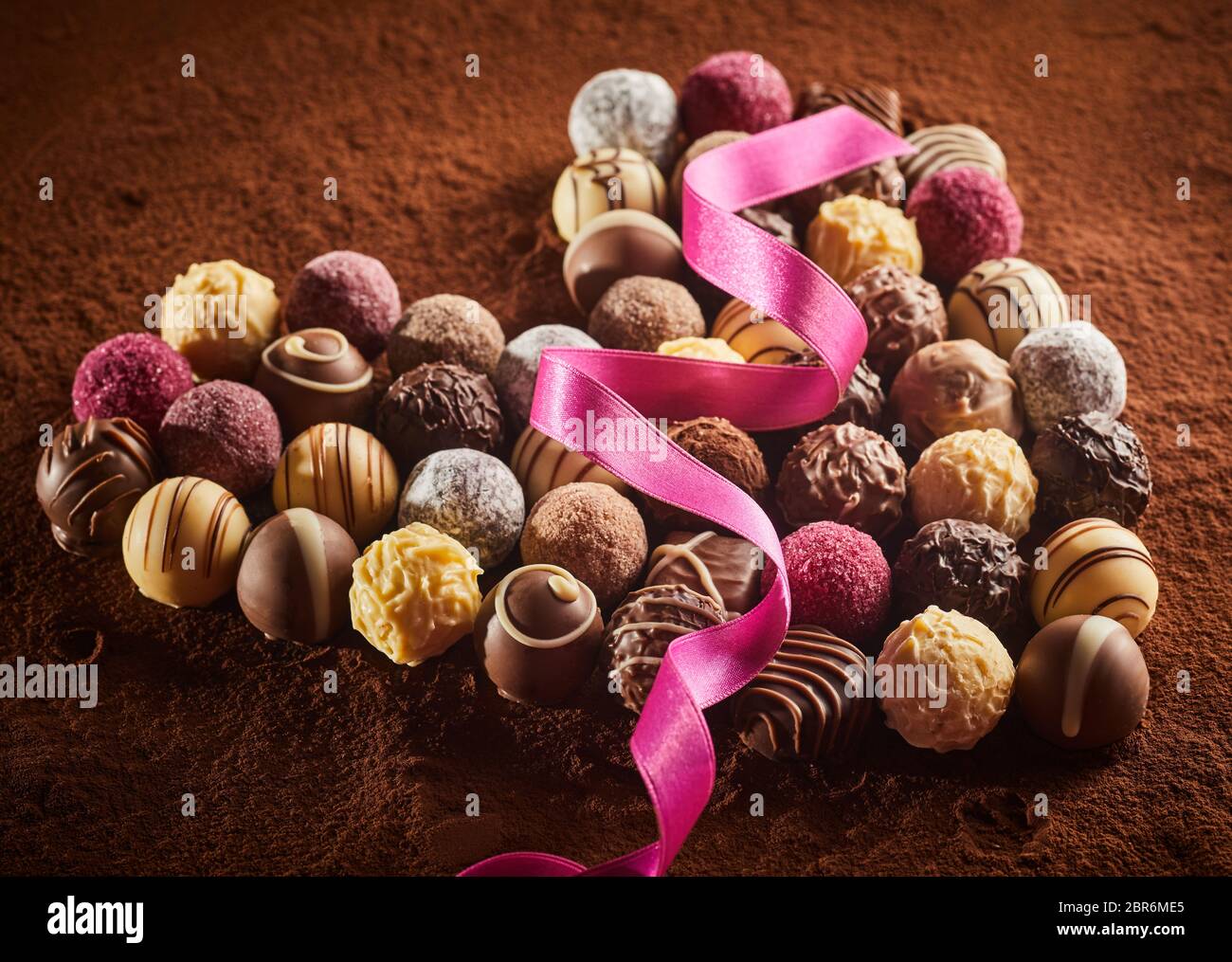 A forma di cuore ad layout di lusso di cioccolatini con il rosa seta nastro sulla polvere di cacao in superficie, visto da vicino da un angolo alto Foto Stock