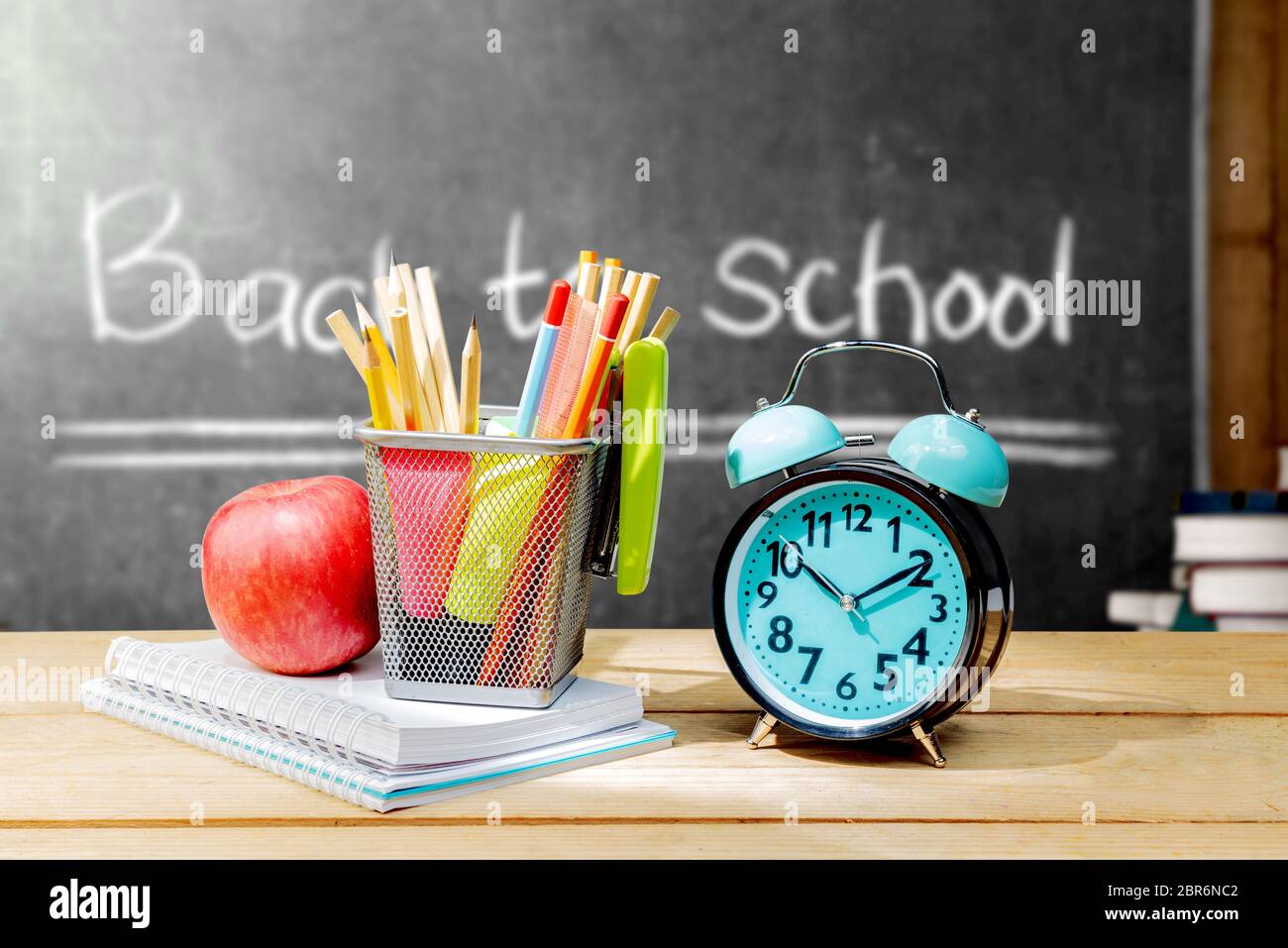 Pila di notebook di Apple e di matite in contenitore a cestello con cucitrice verde e sveglia sul tavolo di legno con blackboard sfondo. Torna t Foto Stock