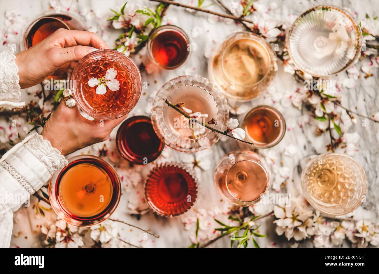 Le donne passano le sfumature offerenti del vino rosa in bicchieri e fiori di primavera fioriti su sfondo bianco, vista dall'alto. Enoteca, bar, degustazione vini, w Foto Stock
