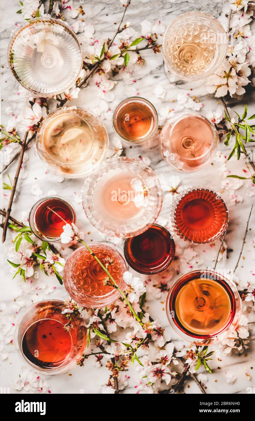 Varie sfumature di vino rosato. Piatto-lay di vino rosa di diversi colori in bicchieri e fiori primavera fiore su sfondo bianco, vista dall'alto. Vino Sho Foto Stock