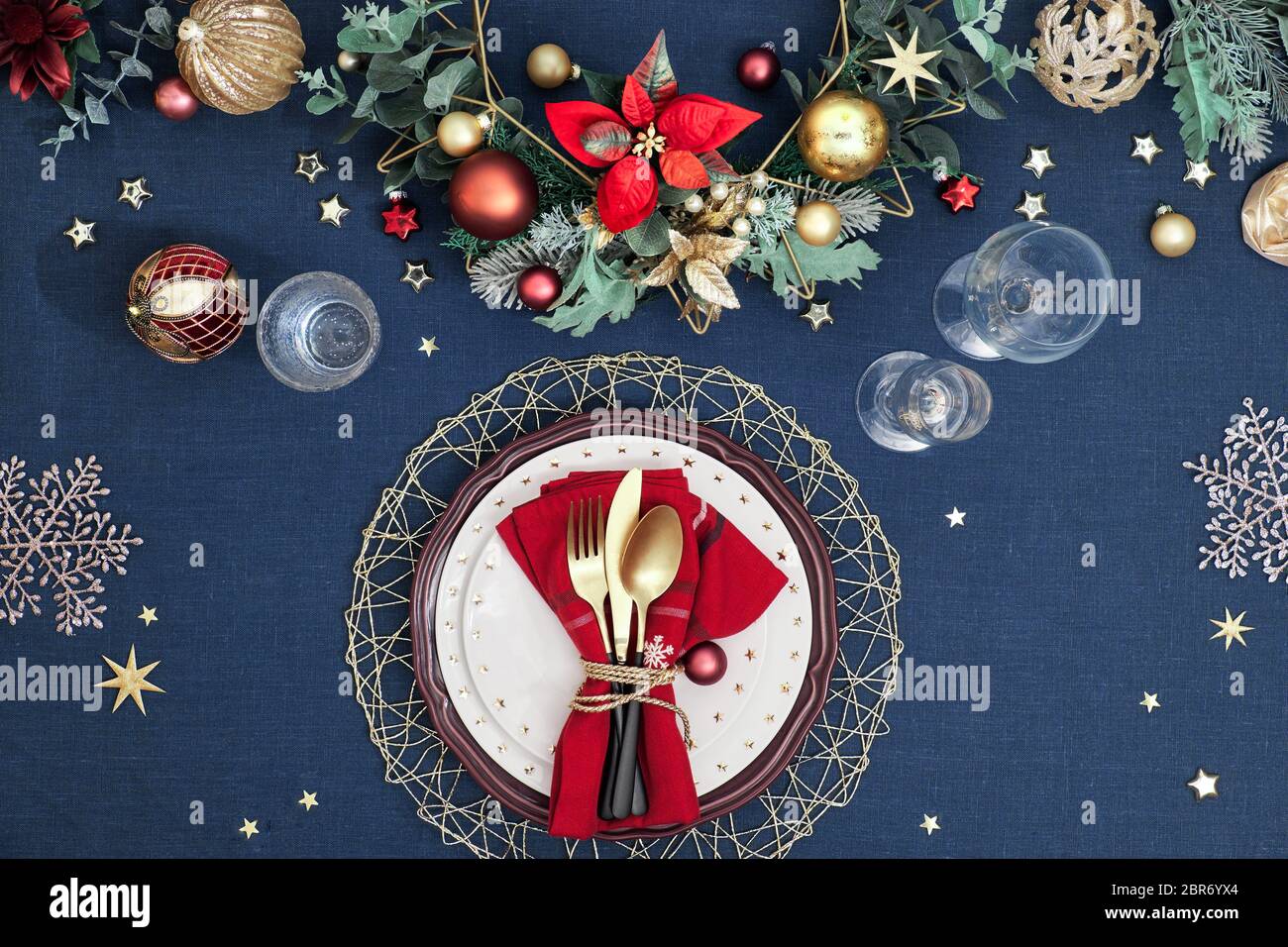 Tavolo di Natale in oro, borgogna e blu scuro. Disposizione piatta, vista dall'alto su tavolo decorativo con posate dorate, piatti bianchi con s. Foto Stock