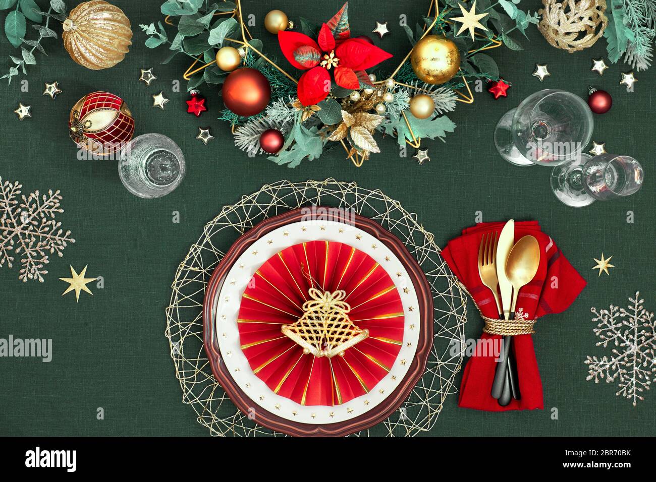 Tavolo di Natale con piatti bianchi di colore rosso scuro, anello di carta rossa e poinsettia, utensili dorati. Decorazioni dorate, rosse, verdi e dorate. Disposizione piatta o Foto Stock