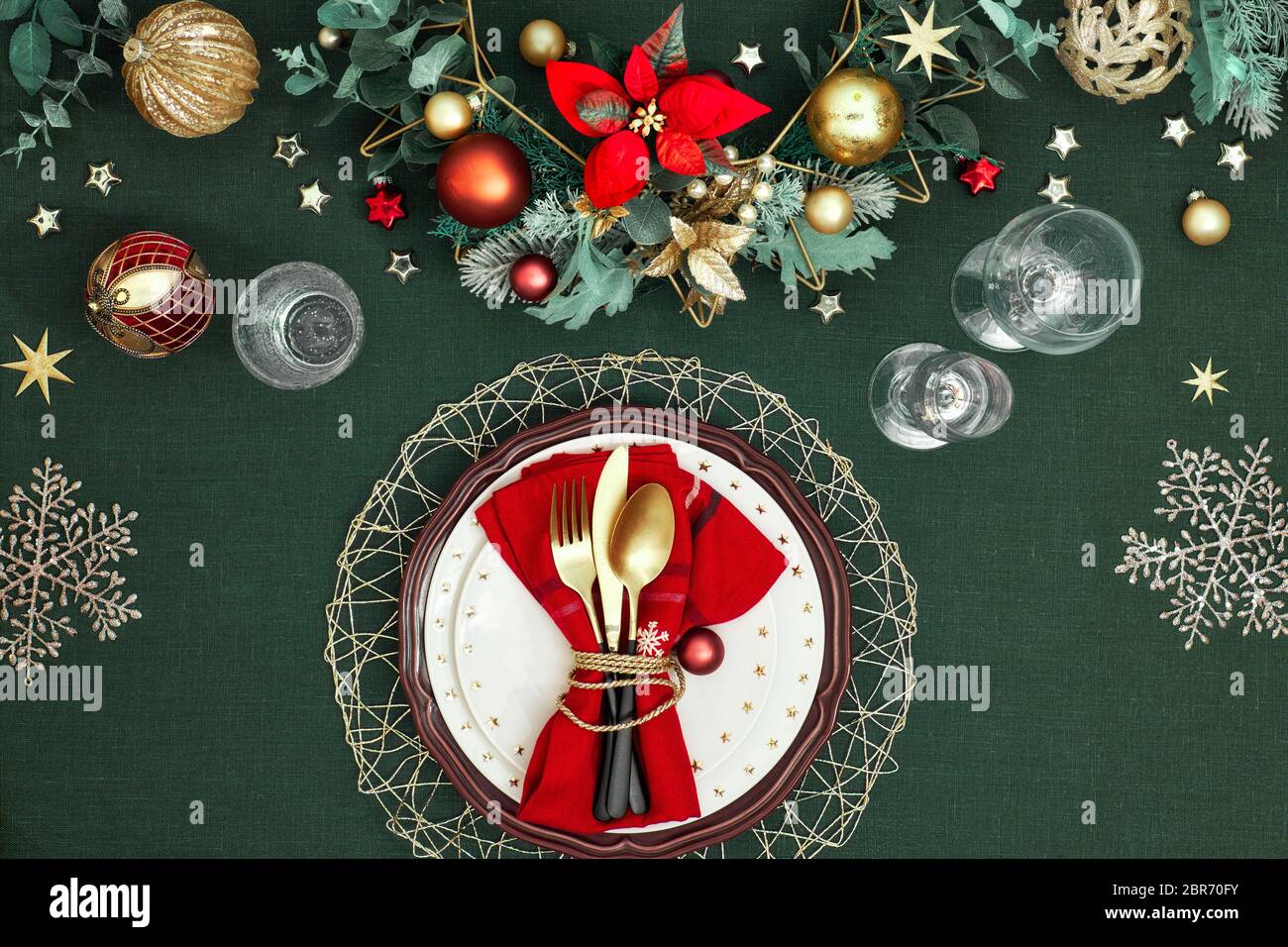 Tavolo di Natale in oro, borgogna e blu scuro. Piatto, vista dall'alto su tavolo decorativo, posate dorate, piatti bianchi con stelle Foto Stock