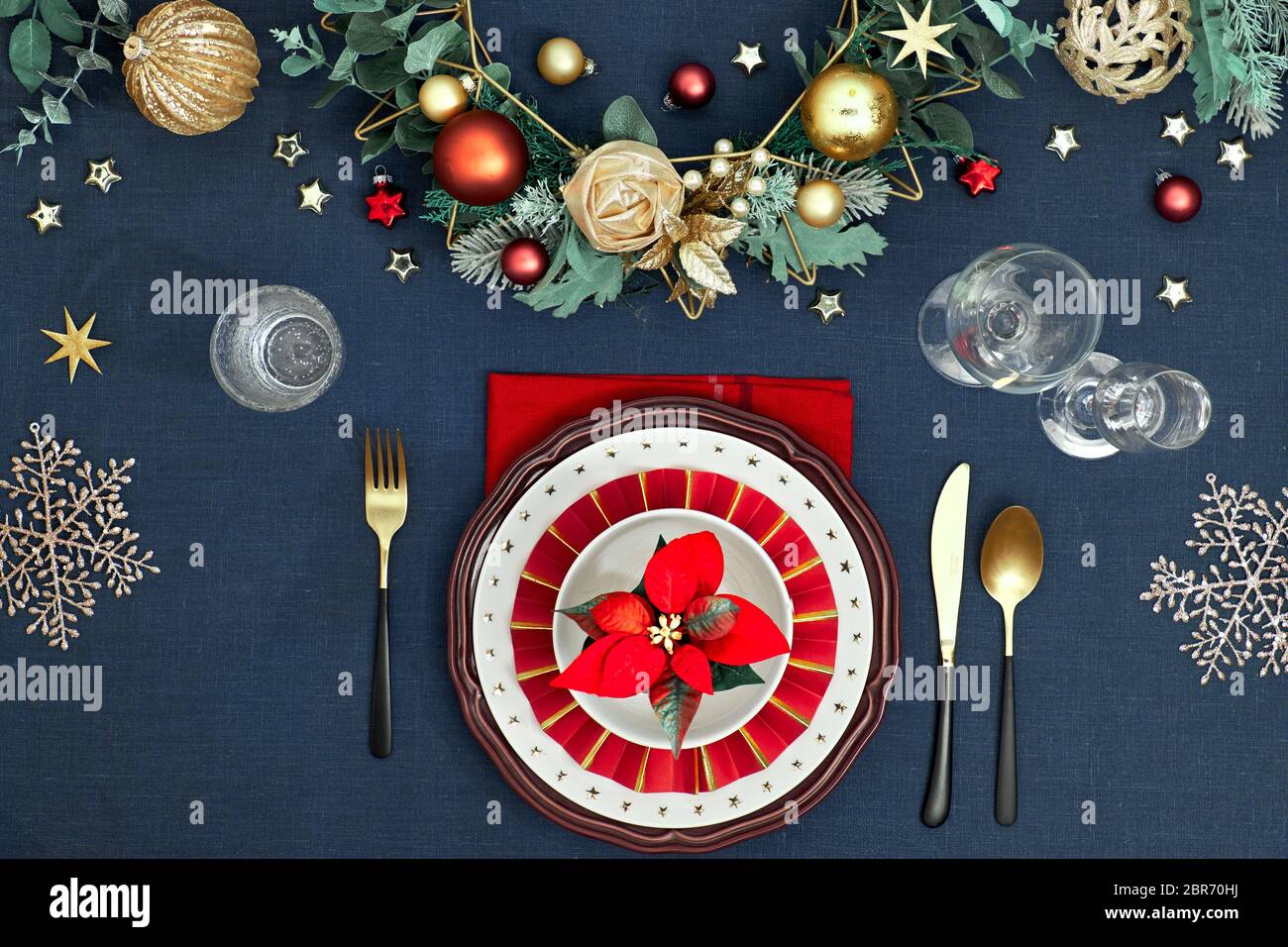 Tavolo di Natale in oro, borgogna e classici blu. Piatto, vista dall'alto su tavolo decorativo, posate dorate, piatti bianchi con st Foto Stock