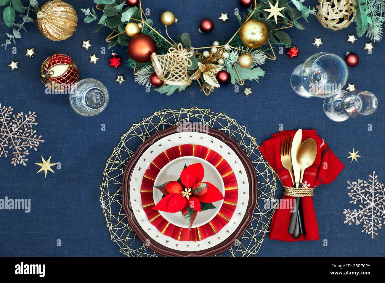 Tavolo di Natale in oro, borgogna e classici blu. Vista dall'alto sul layout del tavolo decorativo, posate dorate, piatti bianchi con stelle. Di sistema Foto Stock