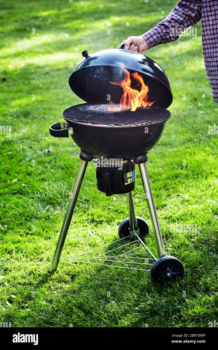 L'uomo il sollevamento del coperchio di un barbecue portatile incendio in  un bollitore grill per