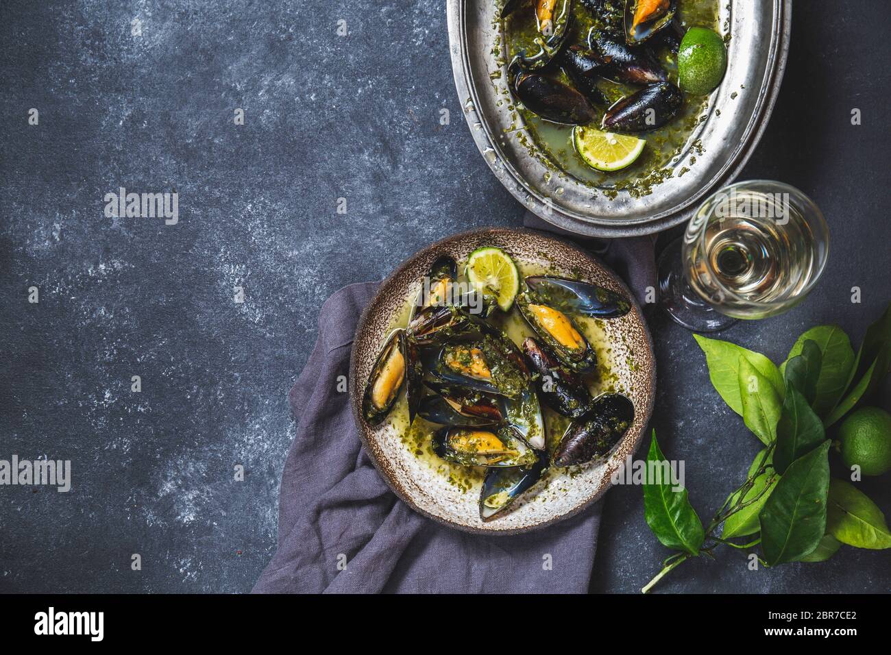 Cozze in erba verde e salsa di vino bianco con limone su fondo scuro. Foto Stock