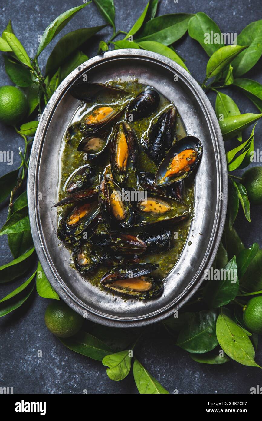 Cozze in erba verde e salsa di vino bianco con limone su fondo scuro. Foto Stock