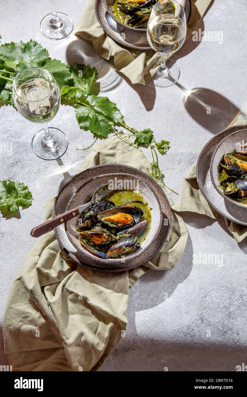 Cena in stile mediterraneo. Primo piano di tavola con cozze in salsa verde e vino bianco. Foto Stock