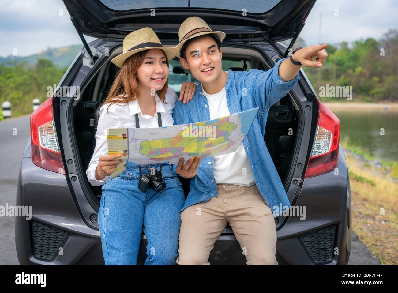 Ritratto di coppia asiatica seduto in auto con l'uomo che punta alla vista e donna che guarda bellissimo paesaggio e tenendo le mappe durante la vacanza insieme in ho Foto Stock