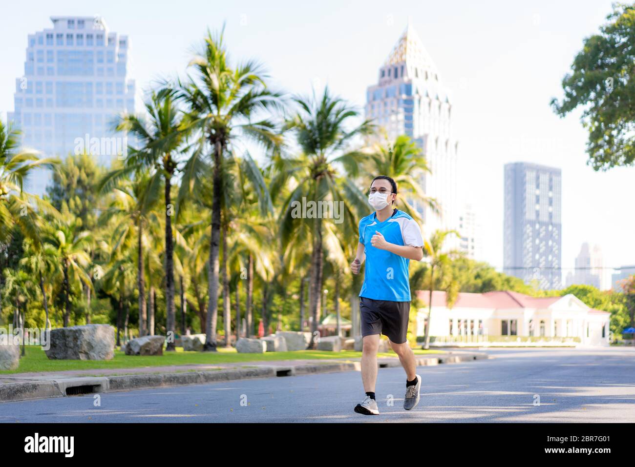 Il giovane asiatico sta facendo jogging ed ecciseing all'aperto nel parco cittadino e indossa la maschera protettiva sul viso per rimanere in forma durante la pandemia di Covid-19 a Bangkok Foto Stock