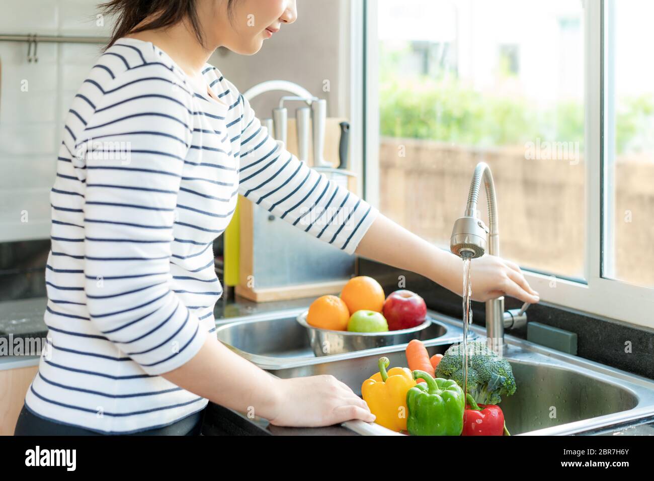 Asian donna sana acqua aperta rubinetto per lavare verdure sopra lavello cucina e pulire una frutta / verdura con acqua per eliminare le possibilità di Foto Stock
