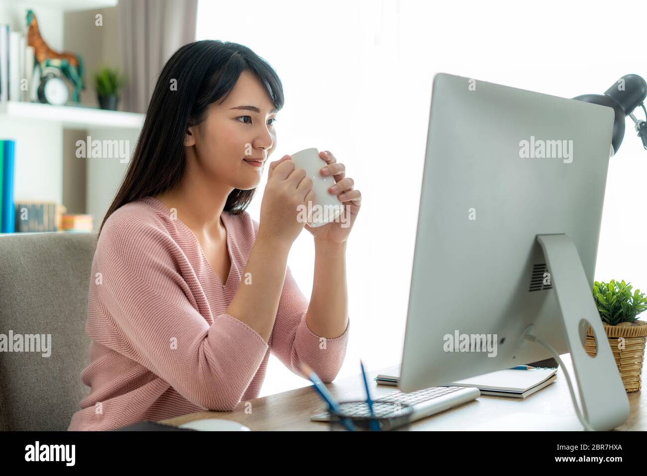 Asian bella giovane donna lavorare da casa lavorare sul computer e bere caffè mentre si lavora in soggiorno a casa. Stile di vita di distanza sociale i Foto Stock