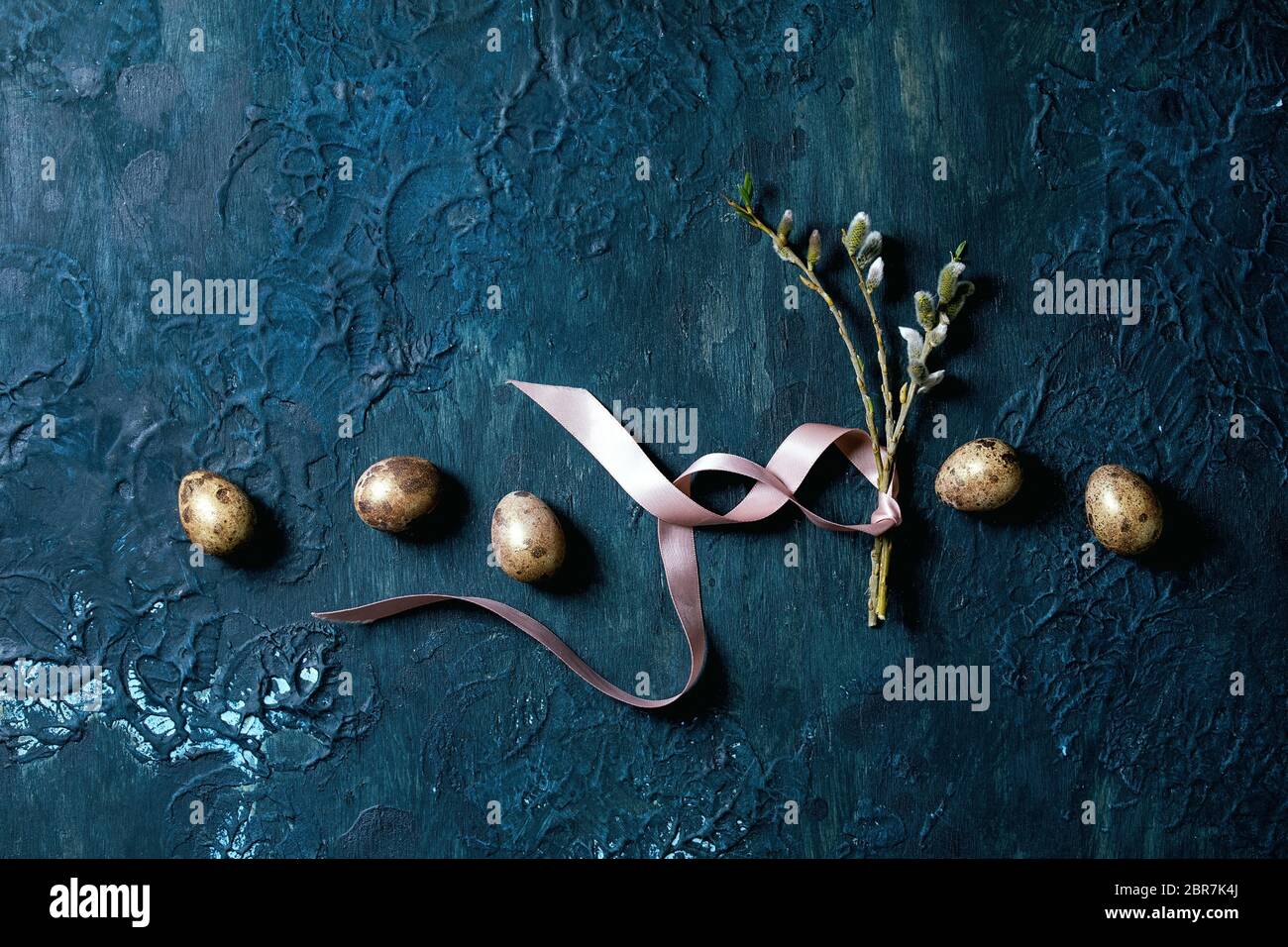 Biglietto di auguri pasquali con rami di salice fiorito, uova di quaglia dorate in fila su sfondo classico blu texture. Disposizione piatta, spazio di copia. Foto Stock